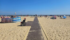 Een strand met een houten looppad naar het water, kleurrijke strandparasols en mensen die ontspannen.