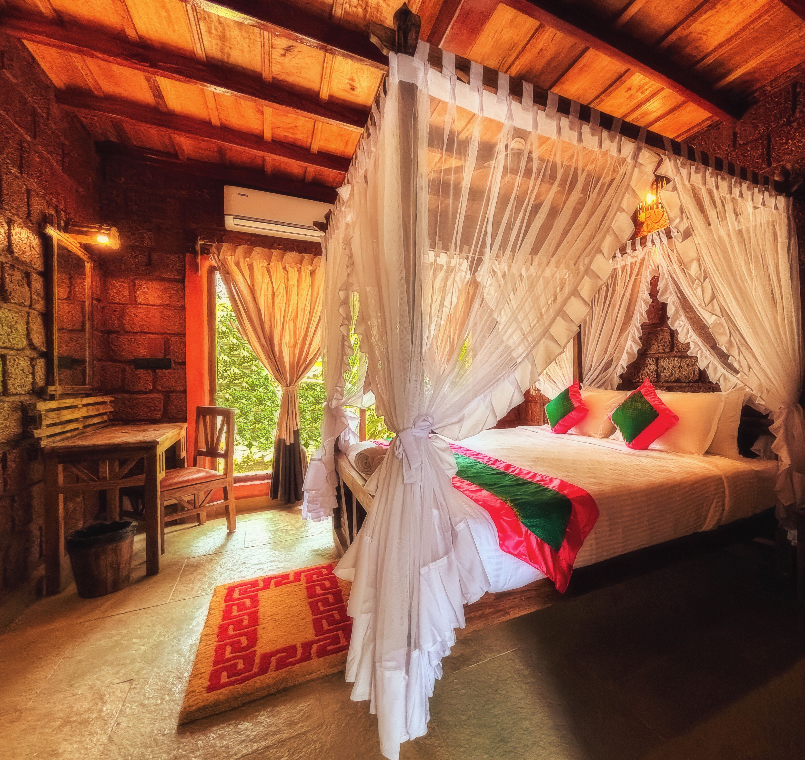A bedroom with a canopy bed, a stone wall, a wooden table, and a chair.