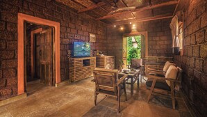 A rustic room with exposed brick walls, wooden furniture, and a television. -  Copper Edge – Eco Resort, Coorg  (Shanivarsanthe)