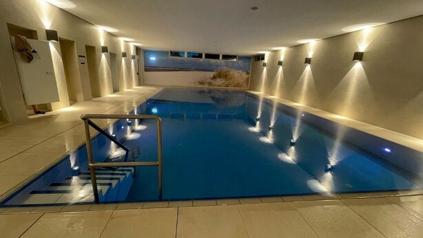 An indoor swimming pool with a glass barrier, tiled floor, and wall-mounted lights. - Modern, cozy, close to the beach - vacation apartment in Cuxhaven, Döse, right on the beach (Cuxhaven)