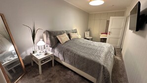 A bedroom with a bed, bedside table, lamp, mirror, wardrobe, and a TV mounted on the wall. - Modern, cozy, close to the beach - vacation apartment in Cuxhaven, Döse, right on the beach (Cuxhaven)