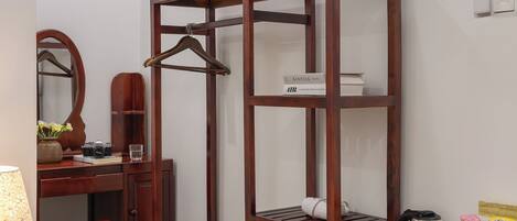 A compact room with a wooden wardrobe, a desk with a mirror, a chair, a small table, and a refrigerator.