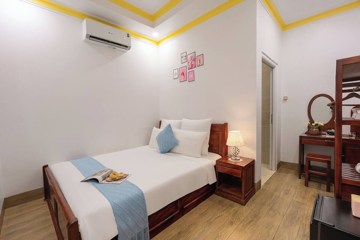 A hotel room with a bed, bedside table, lamp, and a wooden dresser.