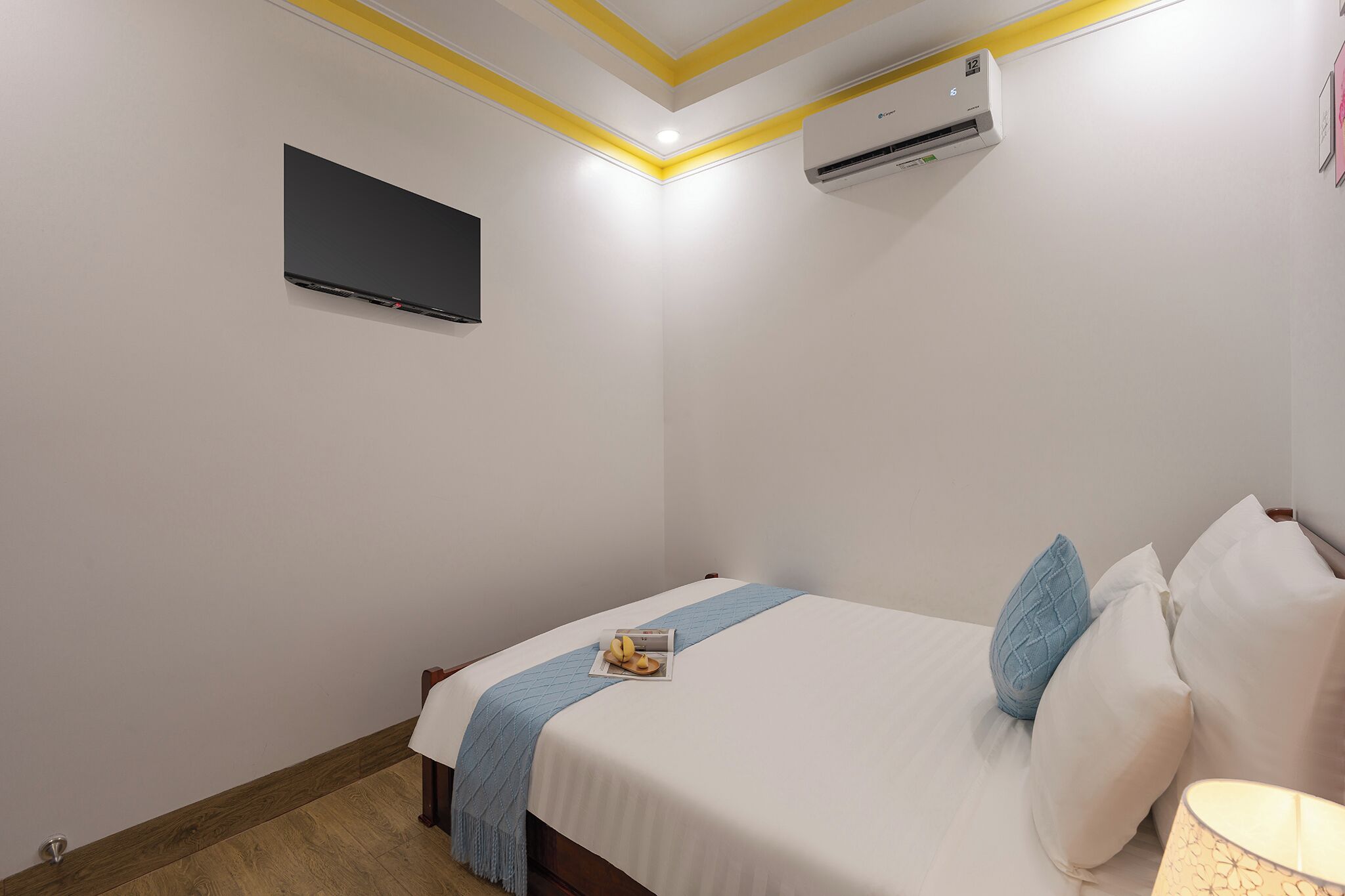 A hotel room with a bed, a flat-screen TV, an air conditioning unit, and a bedside lamp.