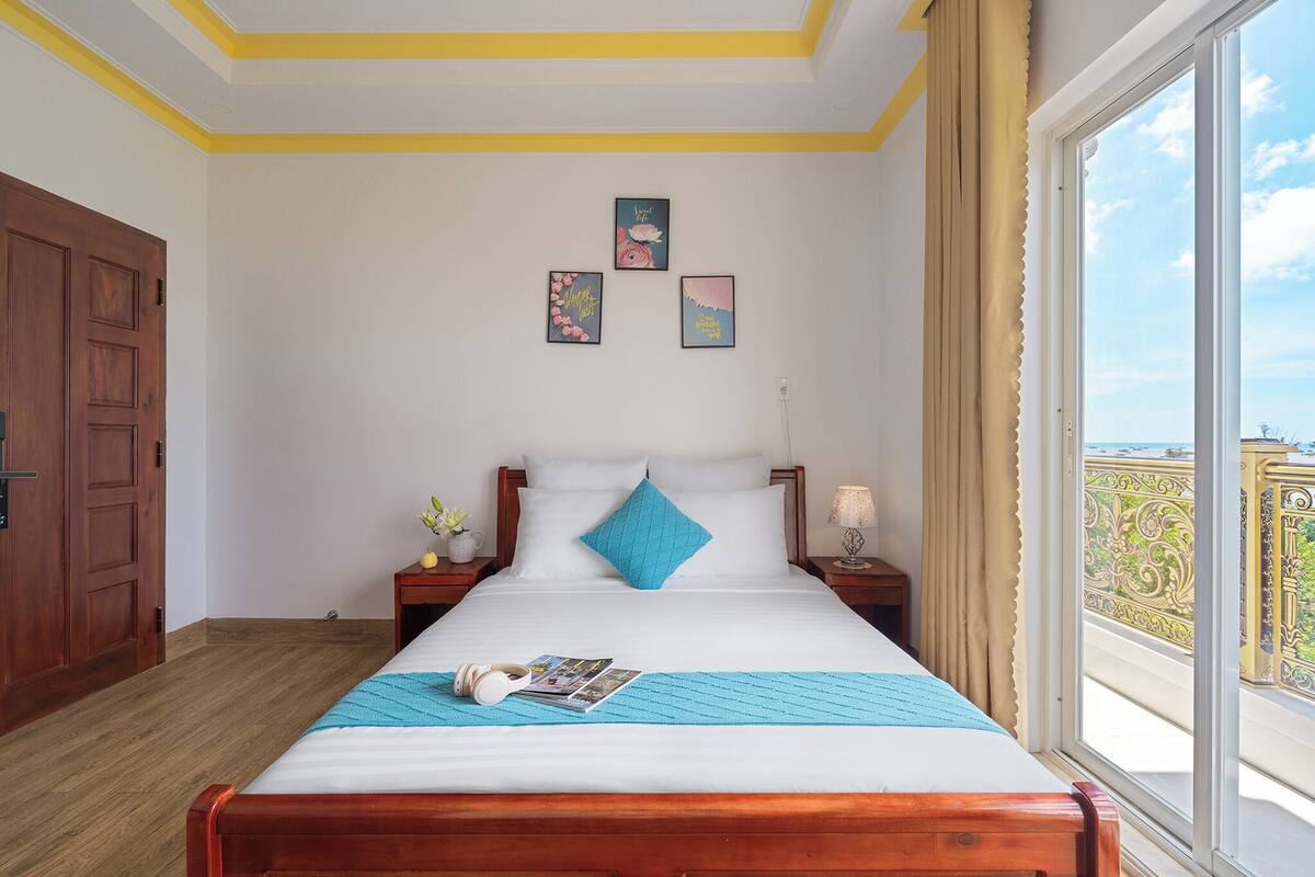 A bedroom with a large bed, a wooden door, and a window with a balcony view.