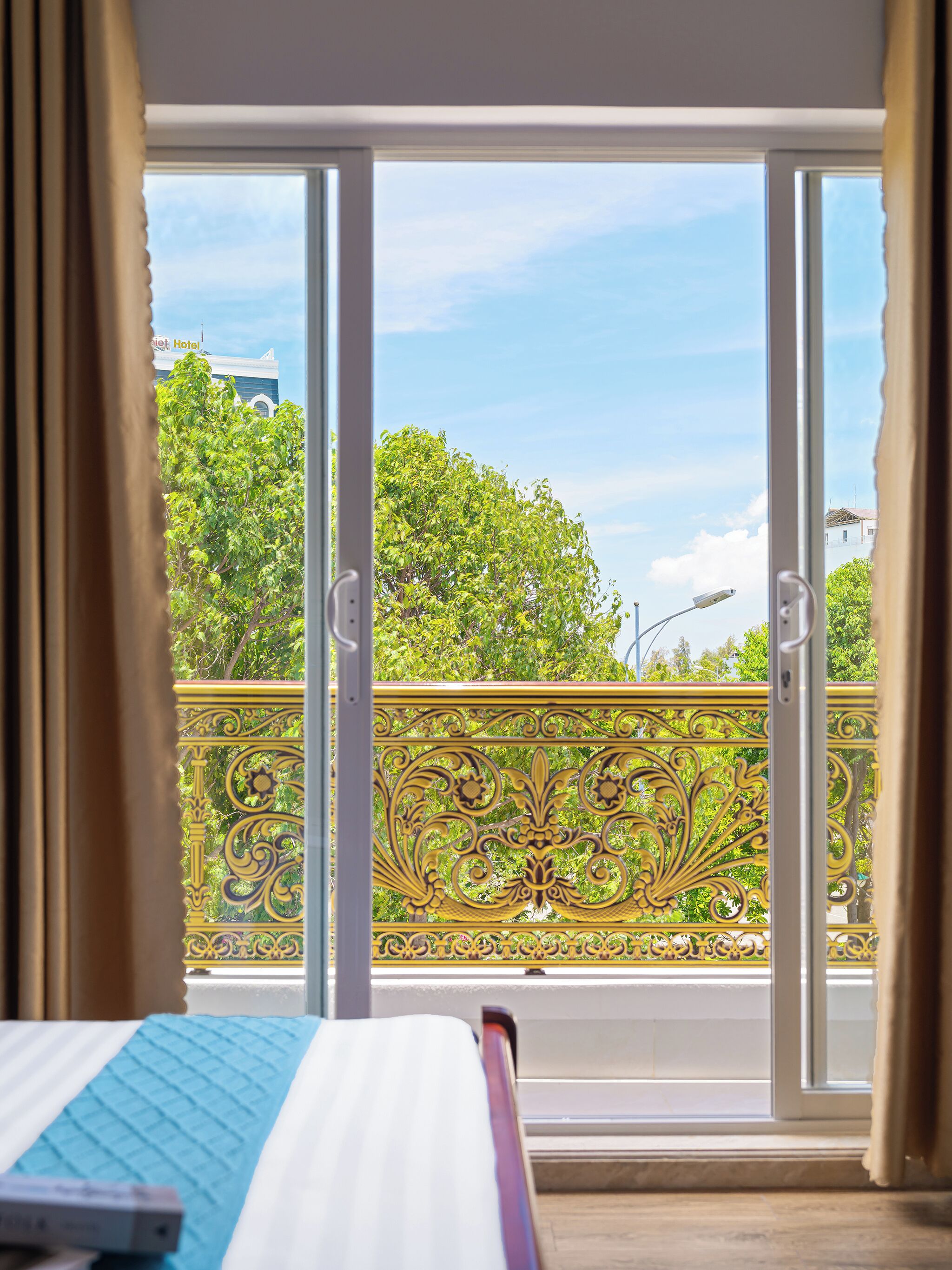 Ein Hotelzimmer mit Bett, Blick auf einen Balkon mit schmiedeeisernem Geländer und blauem Himmel.