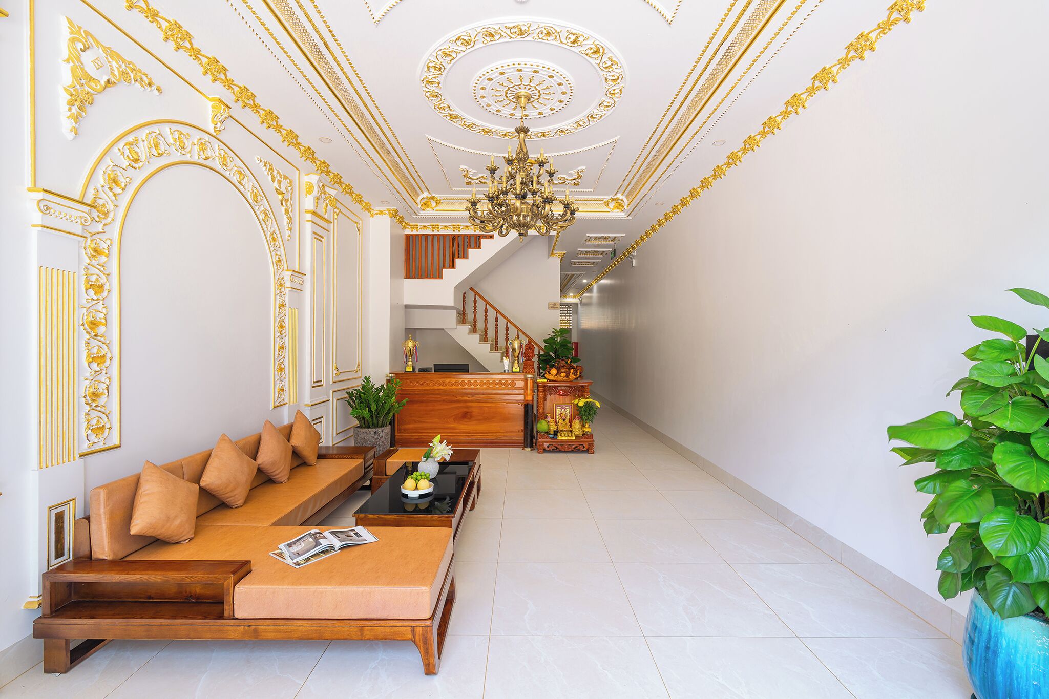A spacious hallway with a grand staircase, a seating area with a sofa and coffee table, and a large potted plant.
