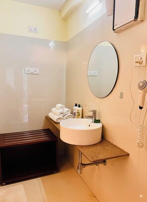 Une salle de bain avec un miroir rond, un lavabo et un banc. On y trouve des serviettes et des articles de toilette sur le comptoir.