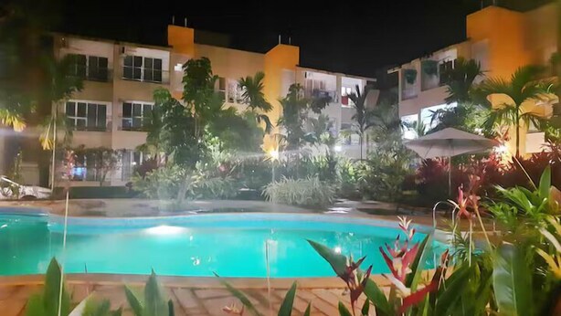 Ein Swimmingpool, umgeben von tropischer Vegetation und einem Gebäude mit Balkonen.