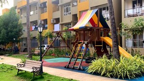 Ein Spielplatz mit Rutsche und Klettergerüsten, umgeben von einer Rasenfläche und Bänken.
