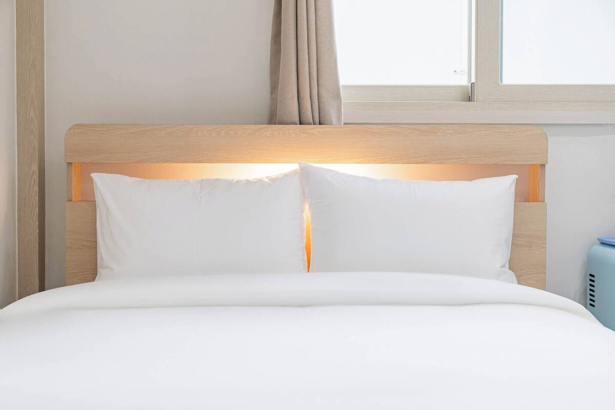 A bed with a wooden headboard, white bedding, and a bedside lamp.
