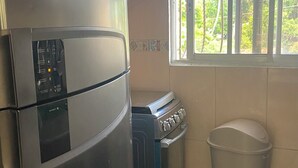 A compact kitchen with a stainless steel refrigerator, a stove, and a window with bars.