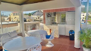 Un patio cubierto al aire libre con mesa y sillas, una lavadora y un bote de basura.