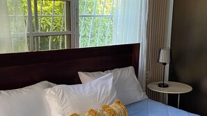 A hotel room with a large bed, a bedside table with a lamp, and a window with curtains.