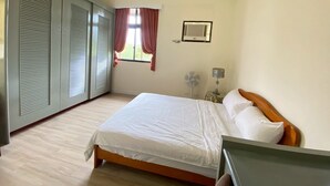 Un dormitorio con cama, ventana con cortinas, aire acondicionado de pared y mesita de noche con lámpara.