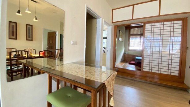 Una habitación amplia con una gran mesa de comedor, un taburete acolchado verde y una puerta corredera de estilo shoji.