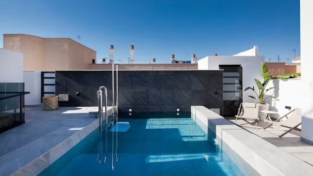 En pool på taket med fri utsikt över himlen, en modern design med en mörk kakelbeklädd vägg och några solstolar.