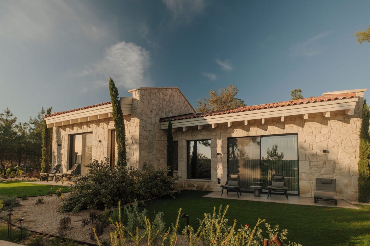 A modern stone house with a patio, outdoor seating, and a well-maintained garden.