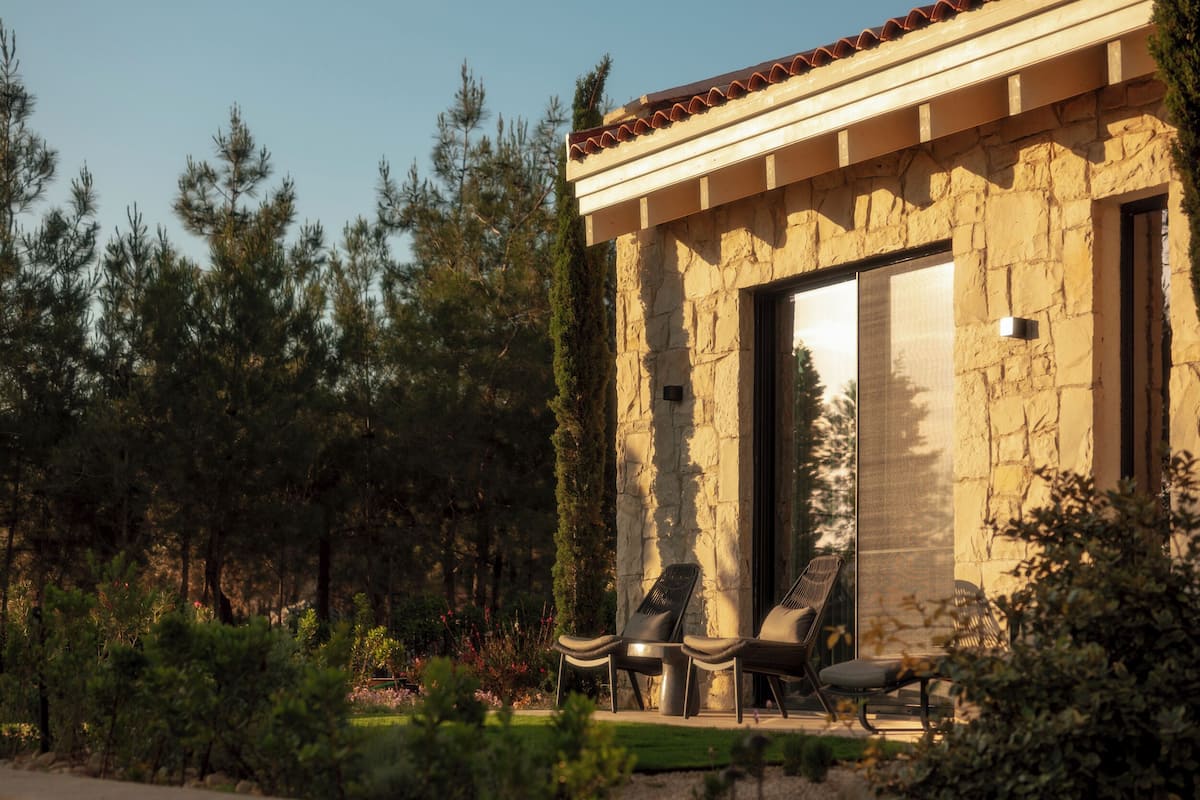 A stone building with a tiled roof, two lounge chairs, and a small table.