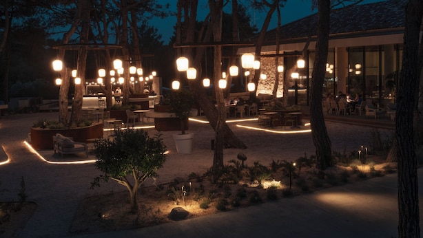 An outdoor dining area with multiple tables and chairs, surrounded by trees and illuminated by hanging lights. - KeyUrla (Urla)