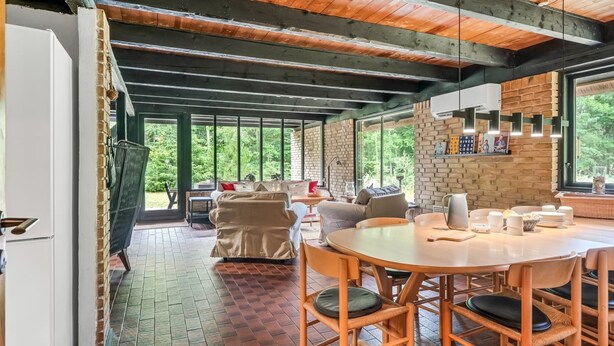 Une pièce spacieuse avec un plafond en bois, des murs en briques, une grande fenêtre et un coin repas comprenant une table et des chaises.