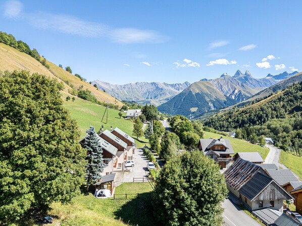 A mountain village with traditional wooden houses, a paved road, and a view of distant mountains.