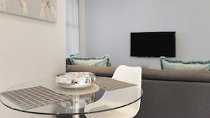 Una sala de estar moderna con una mesa de vidrio, un sofá y un televisor de pantalla plana montado en la pared.