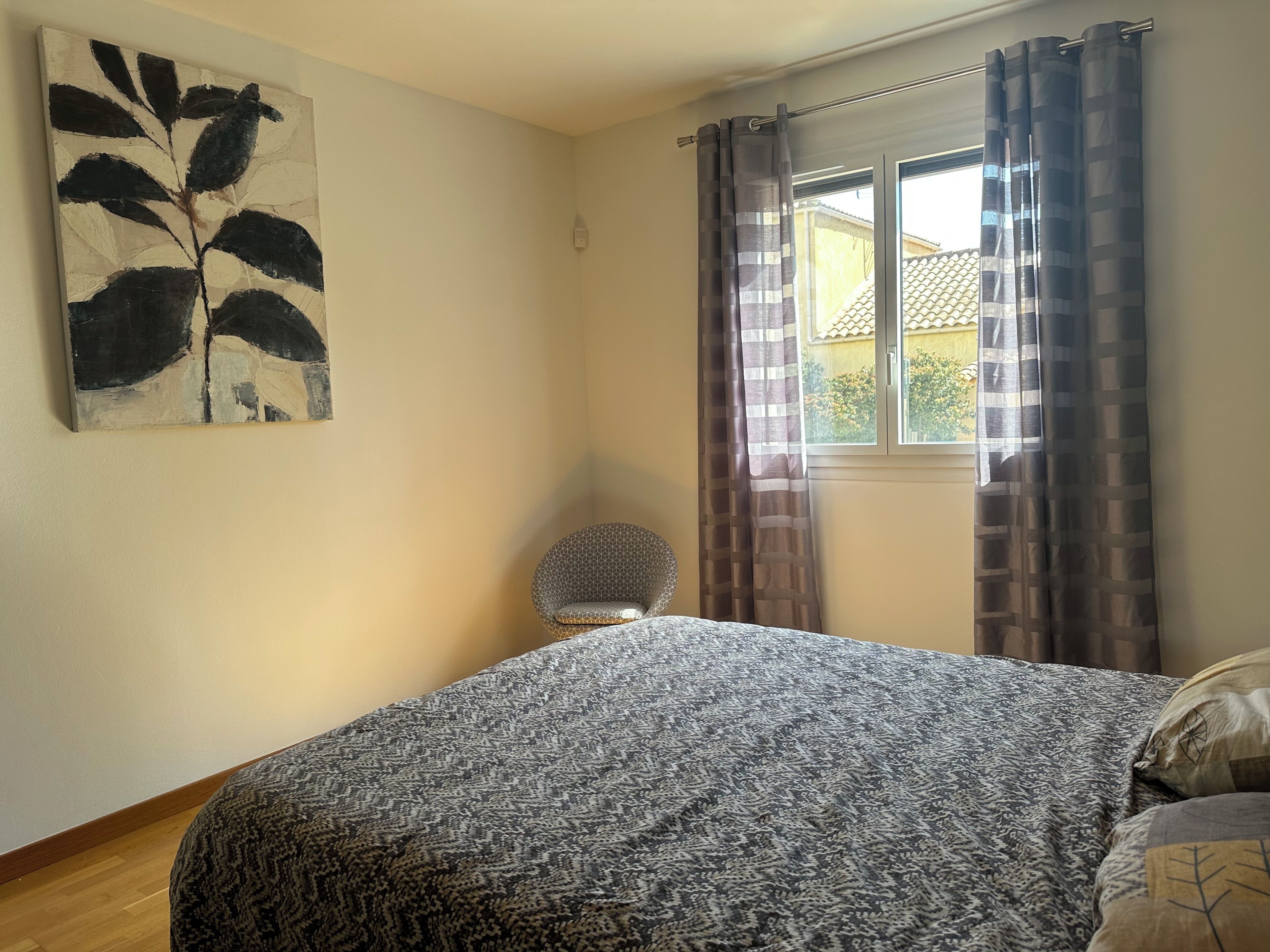 Une chambre à coucher avec un lit, une chaise, une fenêtre avec des rideaux et un tableau au mur.