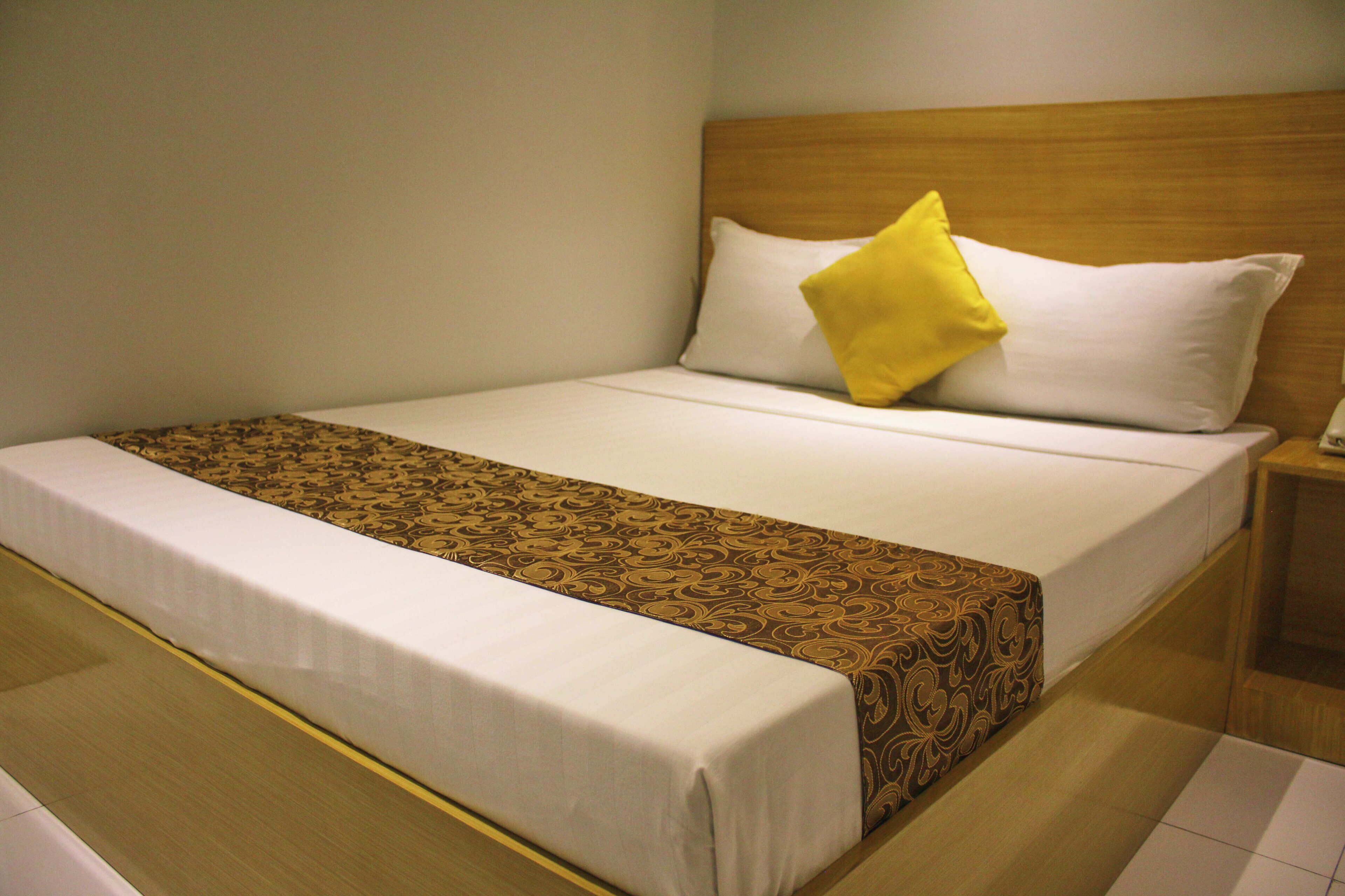 A neatly made bed with a patterned bedspread and a single yellow pillow.