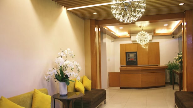 A reception area with a wooden reception desk, a vase of white orchids, and a modern chandelier. - LuxeLite Suites Pasay (Pasay)