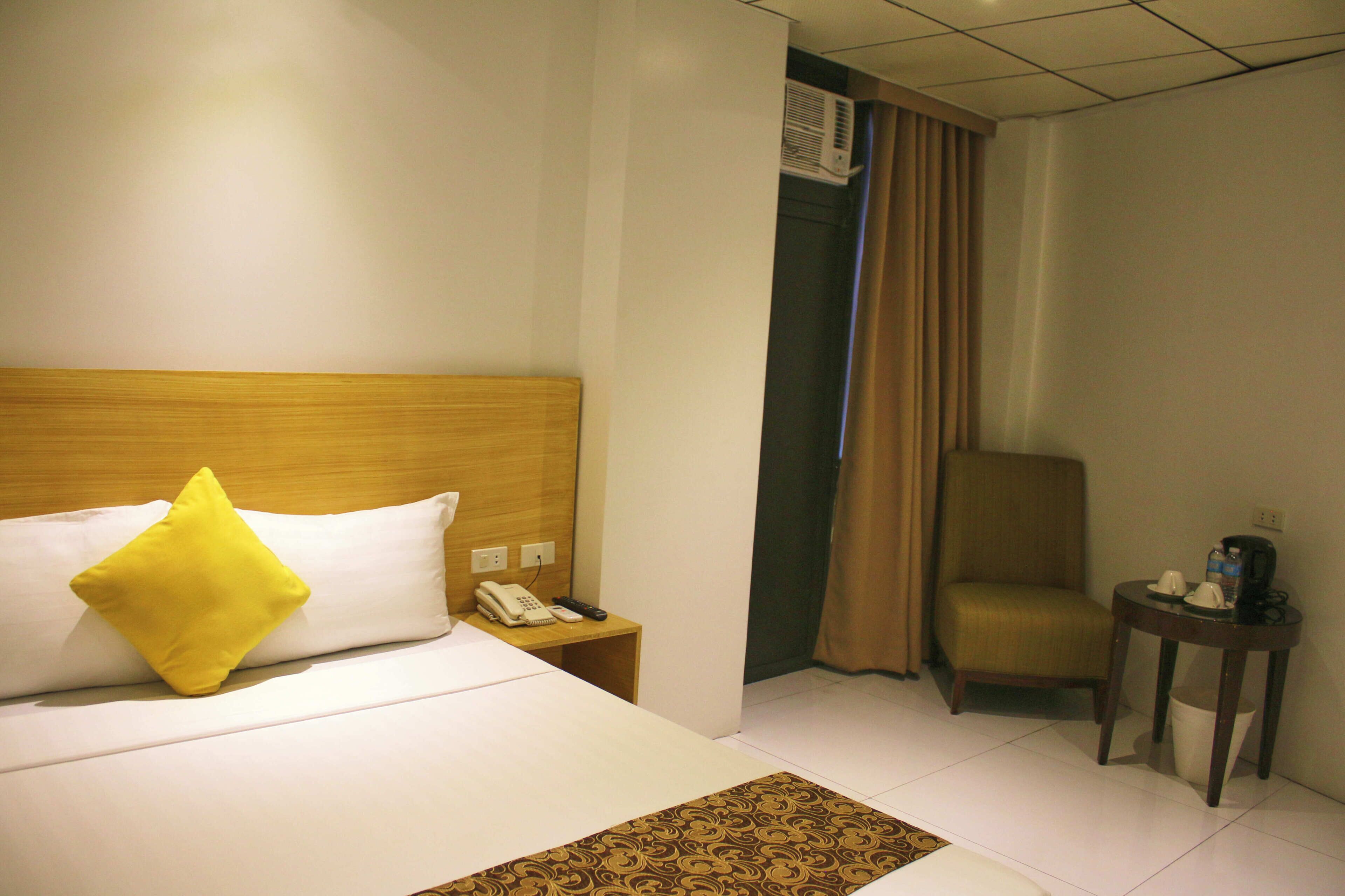 Una habitación de hotel con una cama, una mesita de noche con teléfono, una silla y una pequeña mesa con cafetera.
