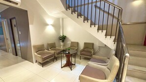 A lobby with a staircase, seating area, and a small table with a plant. - LuxeLite Suites Pasay (Pasay)