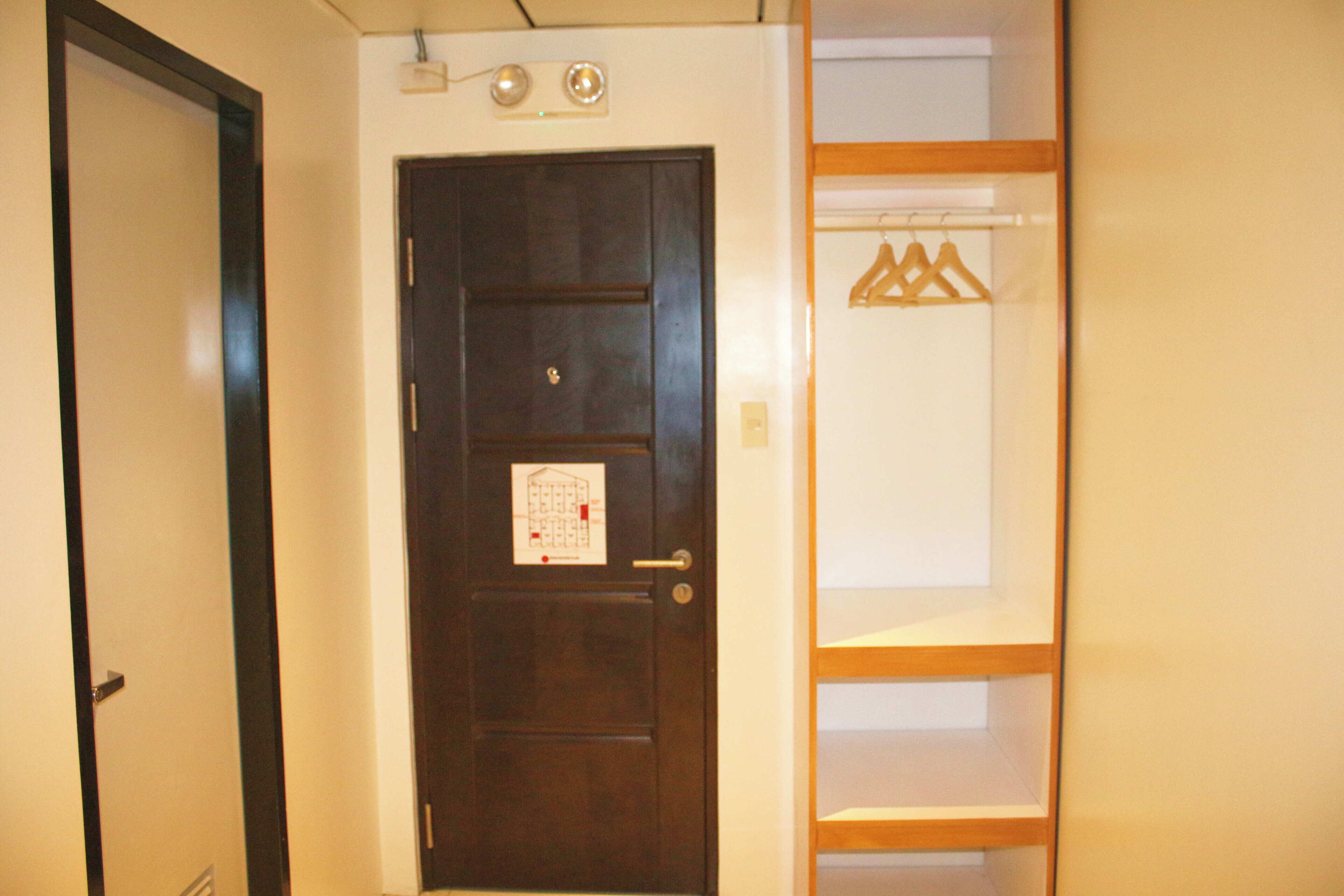 A dark wooden door with a small sign, a white wall, and a wooden shelf with hangers.