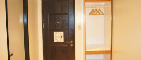 A dark wooden door with a small sign, a white wall, and a wooden shelf with hangers.