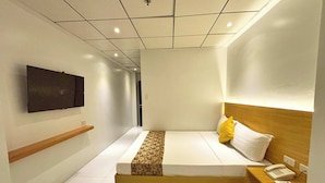 A hotel room with a bed, bedside table, and a mounted TV. - LuxeLite Suites Pasay (Pasay)