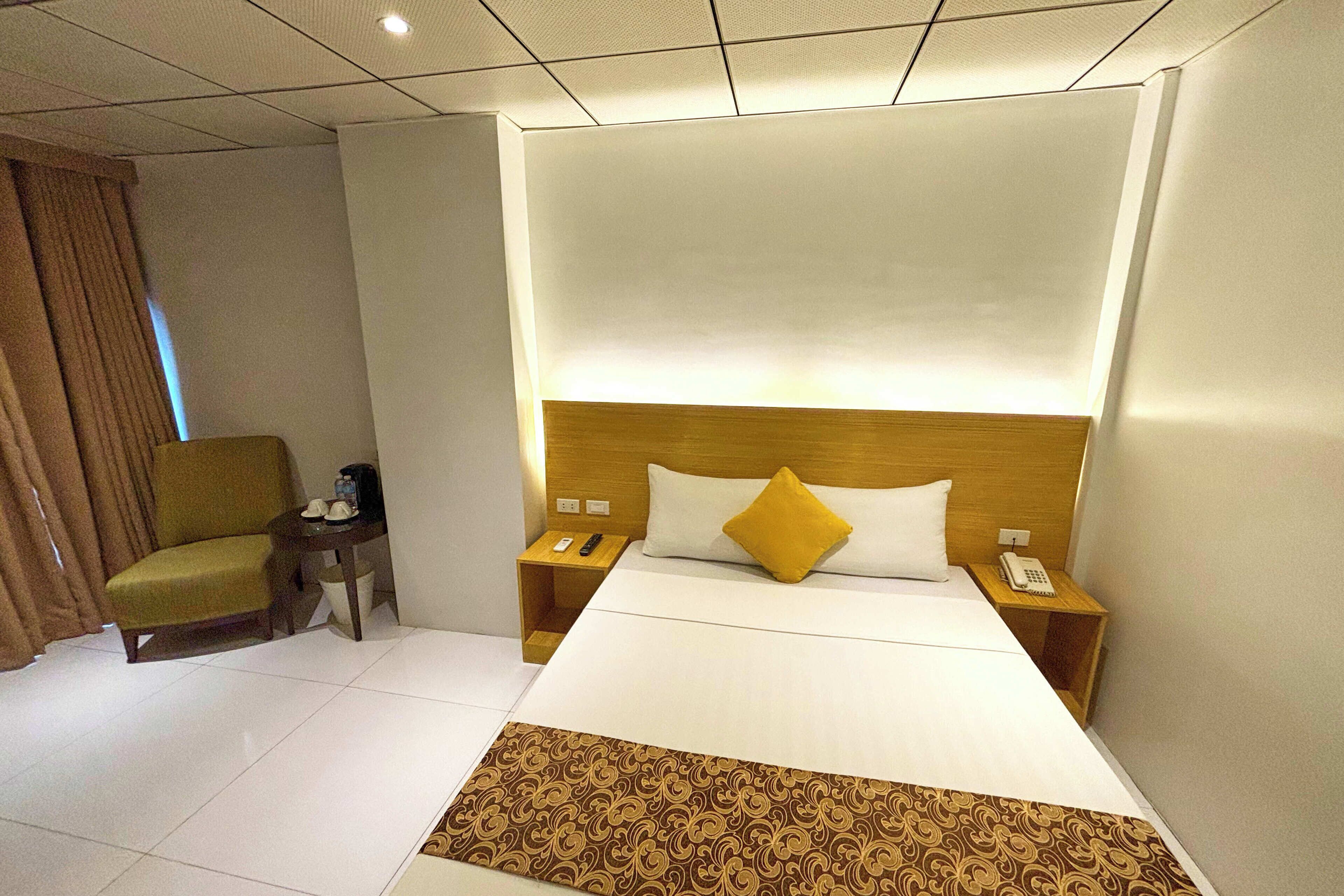 A hotel room with a large bed, two bedside tables, a chair, and a small table with a phone and remote control.