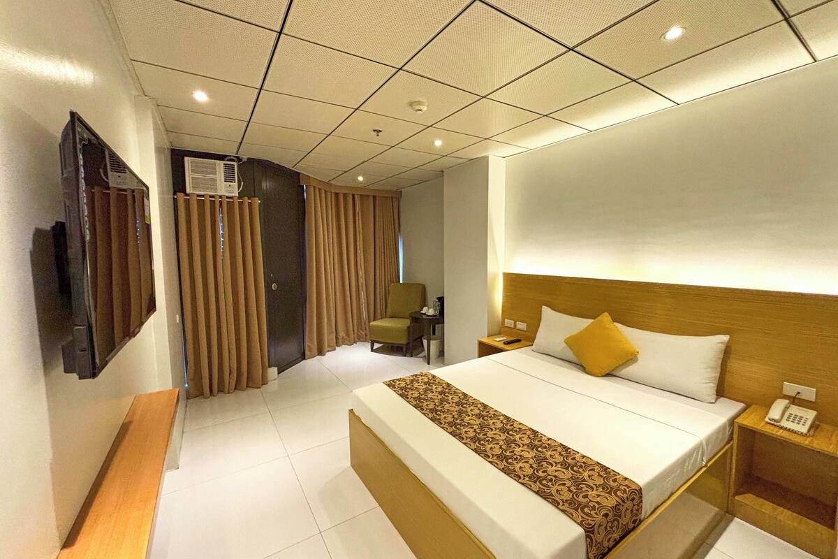 A hotel room with a large bed, bedside table, and a TV mounted on the wall.
