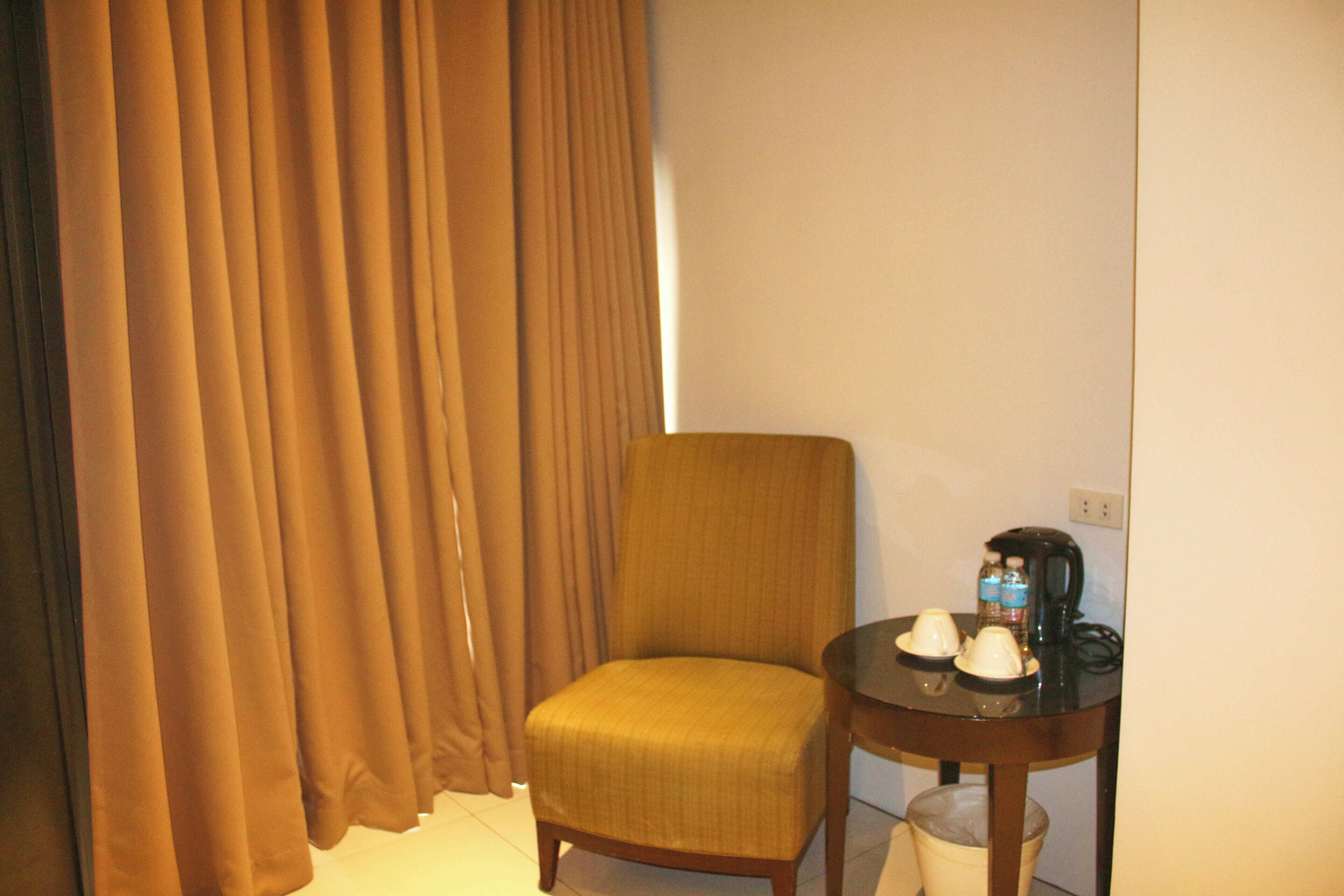 A hotel room with a single chair, a small table with a coffee maker, and a trash bin.