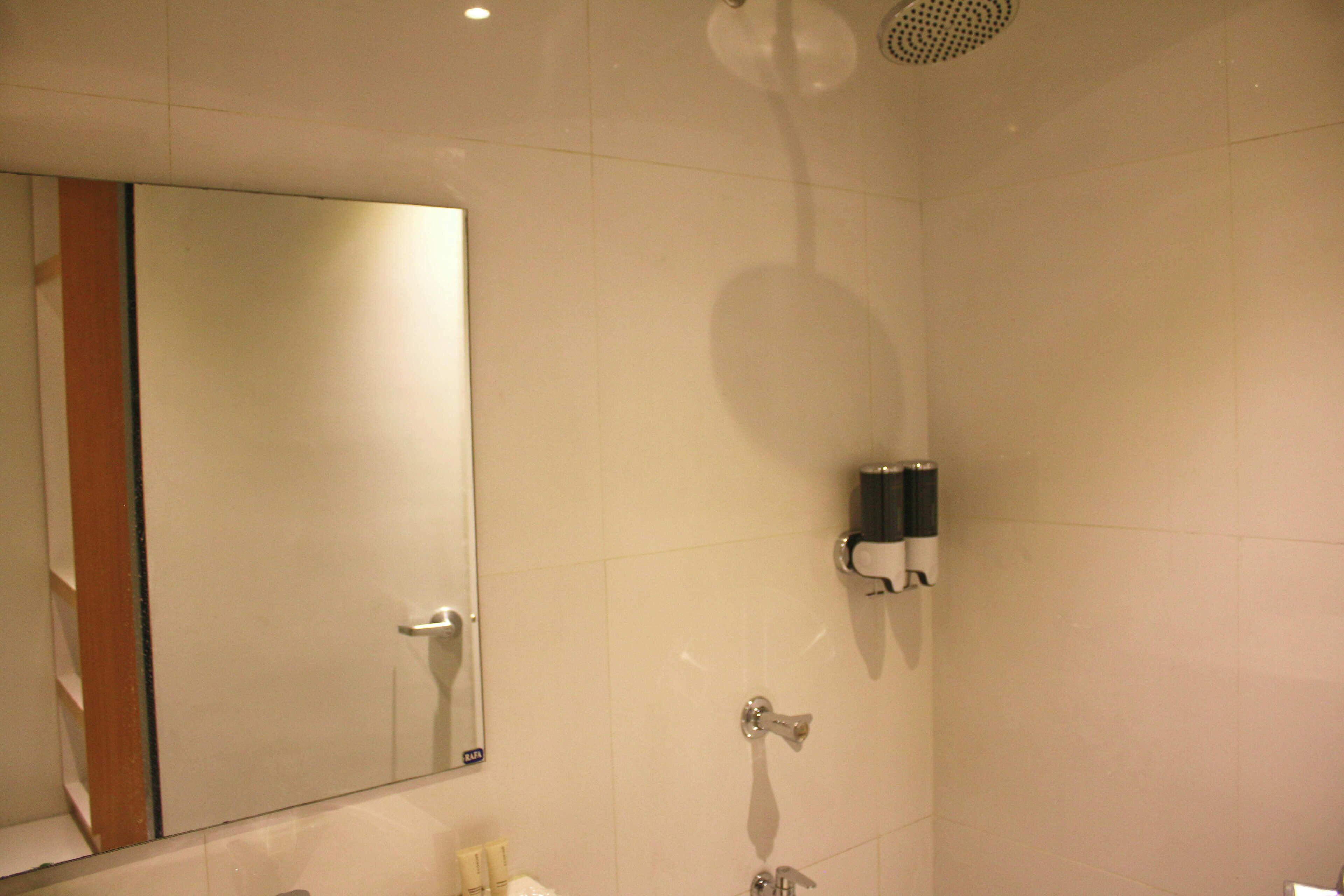 Un baño con un espejo grande, un cabezal de ducha y un perchero para toallas.