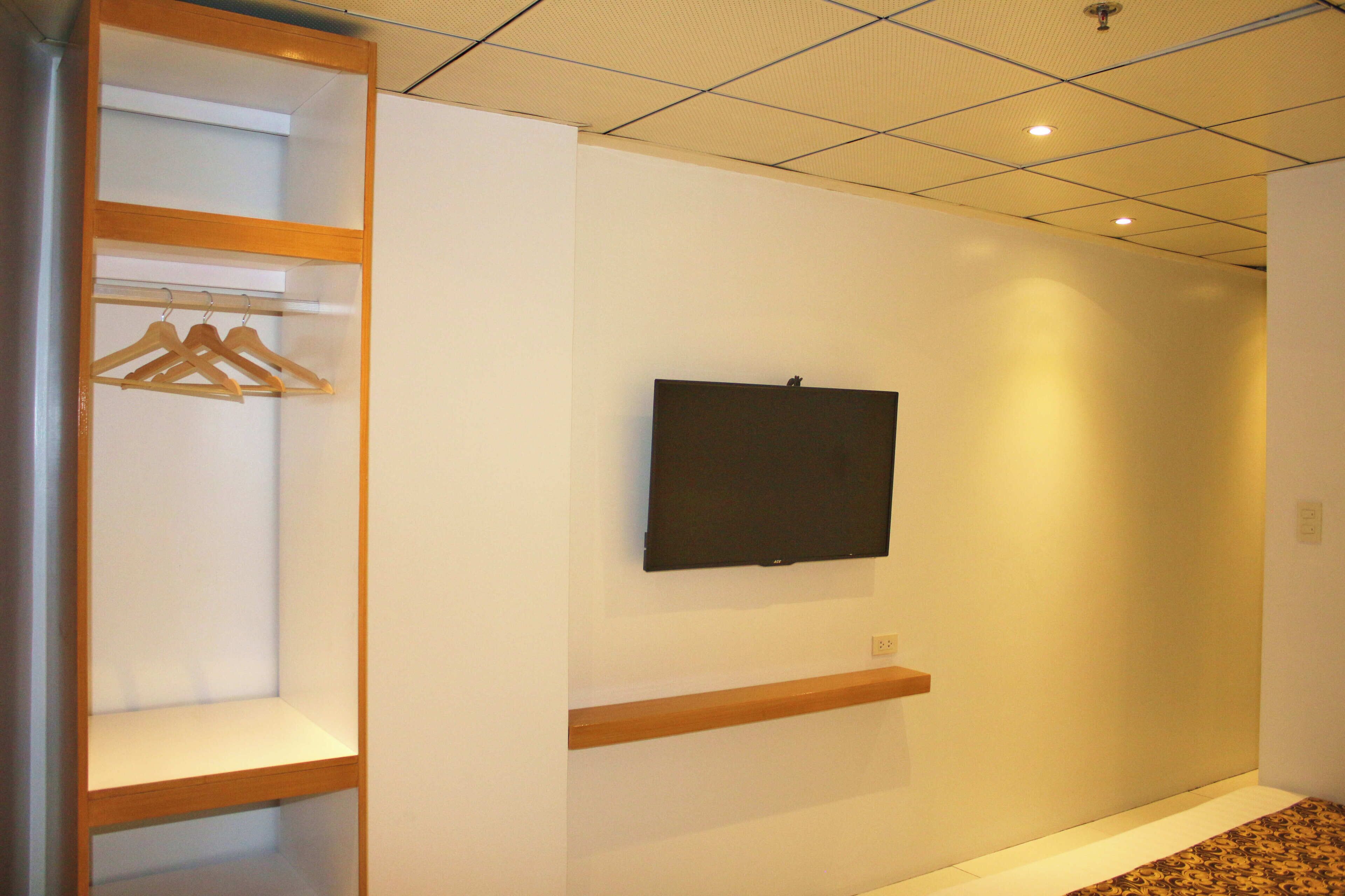 A hallway with a wooden wardrobe, a mounted television, and a patterned carpet.