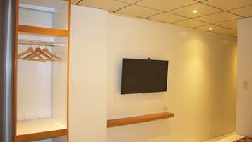 A hallway with a wooden wardrobe, a mounted television, and a patterned carpet.