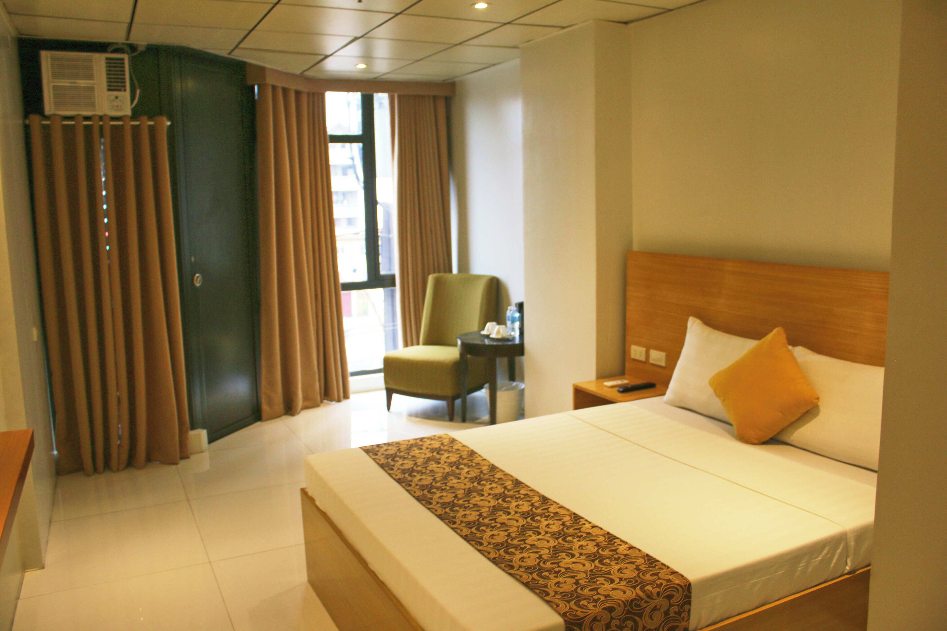 A hotel room with a large bed, a chair, a desk, and a window with curtains.