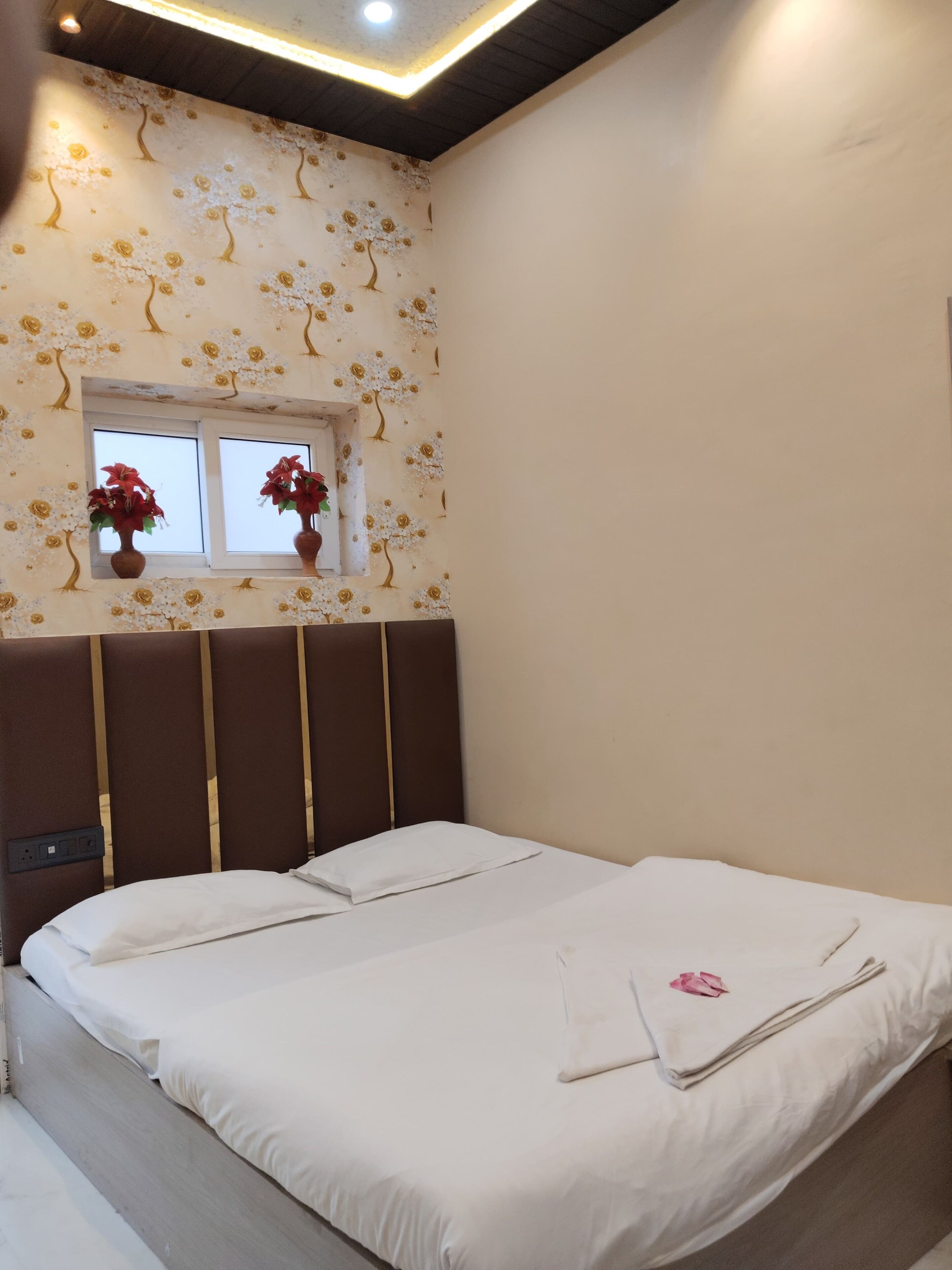 A hotel room with a bed, a window with flowers, and a ceiling light.