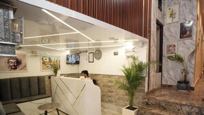 A reception area with a reception desk, seating, a TV, and a wall with framed pictures. - Shree Shiven Homestay (Varanasi)