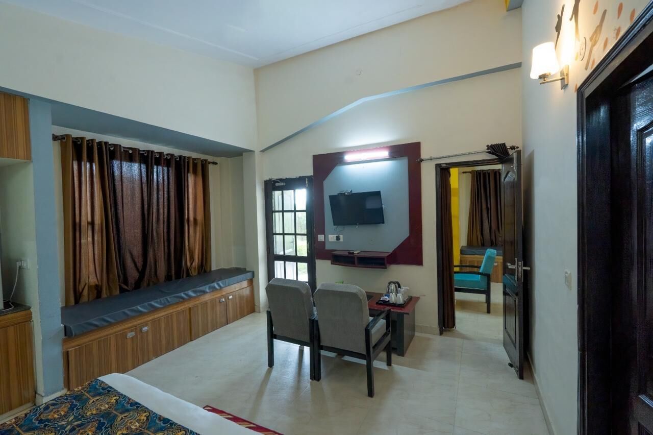 A hotel room with a bed, a desk with a chair, a TV mounted on the wall, and a window with curtains.