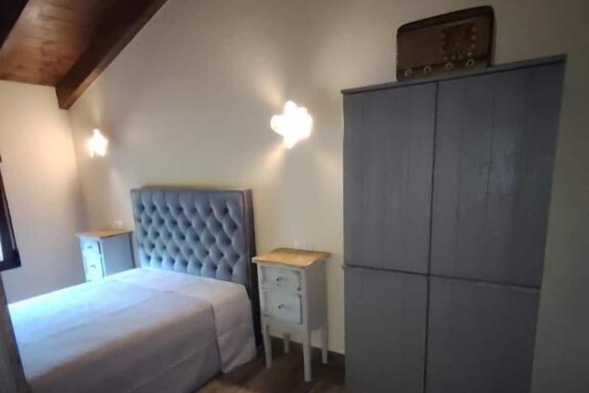 A bedroom with a bed, a nightstand, a dresser, and two wall-mounted lights.