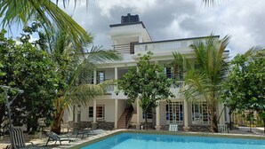 A two-story house with a swimming pool, surrounded by palm trees and a clear sky.