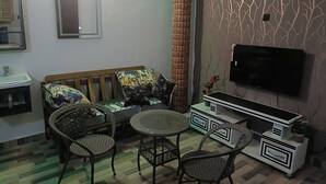 A living room with a sofa, two chairs, a small round table, a TV, and a decorative wall.