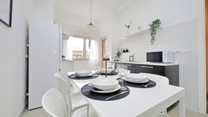 A modern kitchen with white cabinets, a microwave, and a sink. There is a dining table set with plates, glasses, and cutlery.