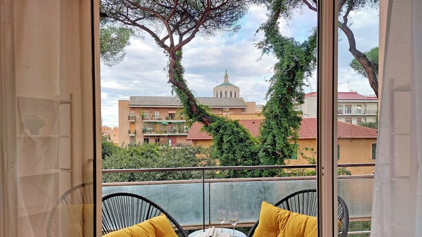 A balcony with two black wicker chairs, each with a yellow cushion, and a small round table with two wine glasses and a book.